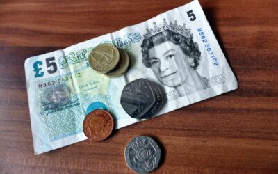 A five pound note with a collection of coins on top