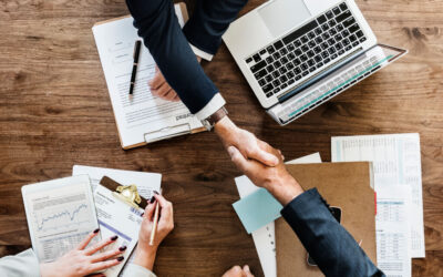 Two people shaking hands over desk with contract