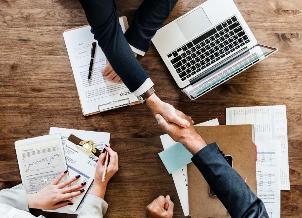Two people shaking hands over desk with contract