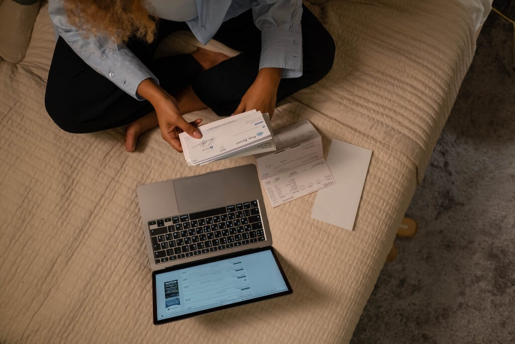 Person looking at a stack of cheques with a laptop