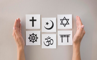 Two hands placing pieces of paper with the symbols of the six major religions on a table