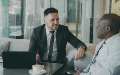 Two business men talking in a glass box office with a laptop on a coffee table