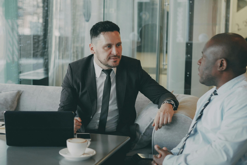 Two business men talking in a glass box office with a laptop on a coffee table